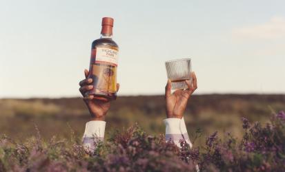 Two hands appearing out of heather, one with a Highland Park 18 Year Old bottle and the other holding a glass of whisky