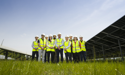 A group of people wearing high visibility vests stand next to a series of solar panels