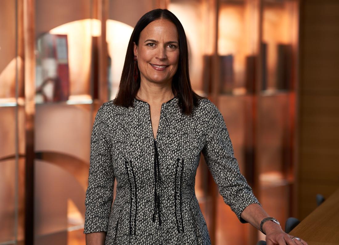 Image of female standing with hand placed on table in front of copper background
