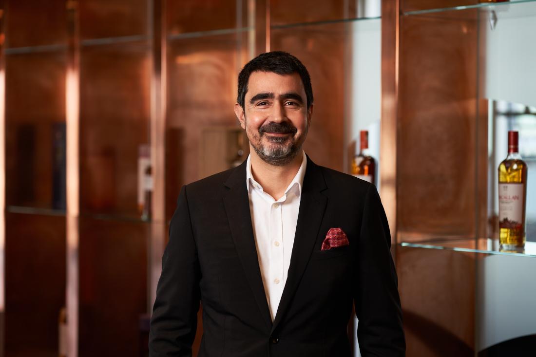 Man in black suit and white shirt smiling and standing in front of a copper wall