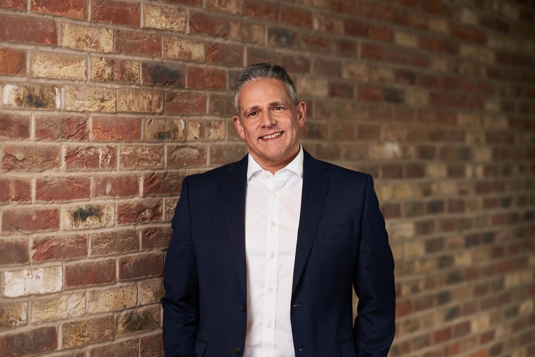 Man in a suit smiling in front of a red brick wall
