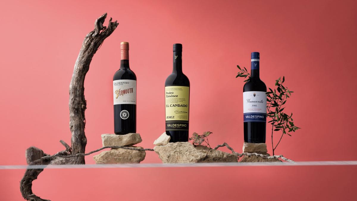 Three Valdespino sherry and vermouth bottles in front of a light red background