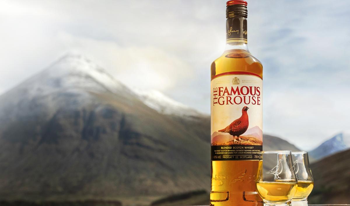 A bottle of The Famous Grouse and two whisky glasses in front of a snow capped mountain