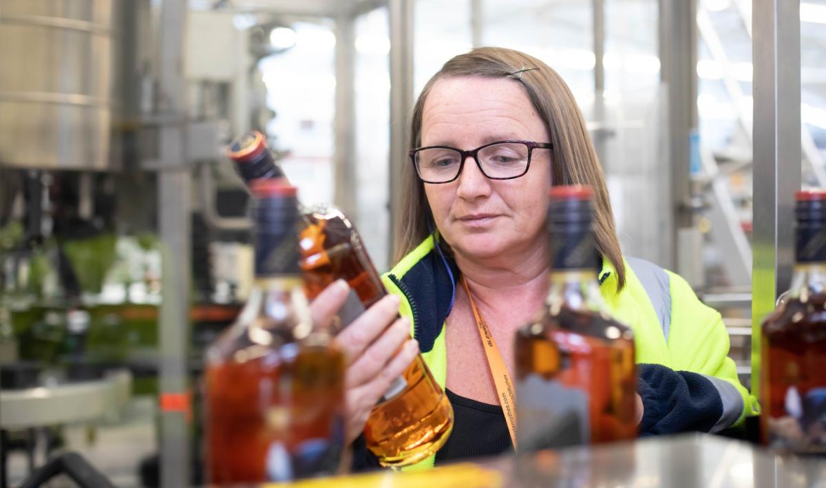 A female colleague holds a bottle of The Famous Grouse and inspects the label 