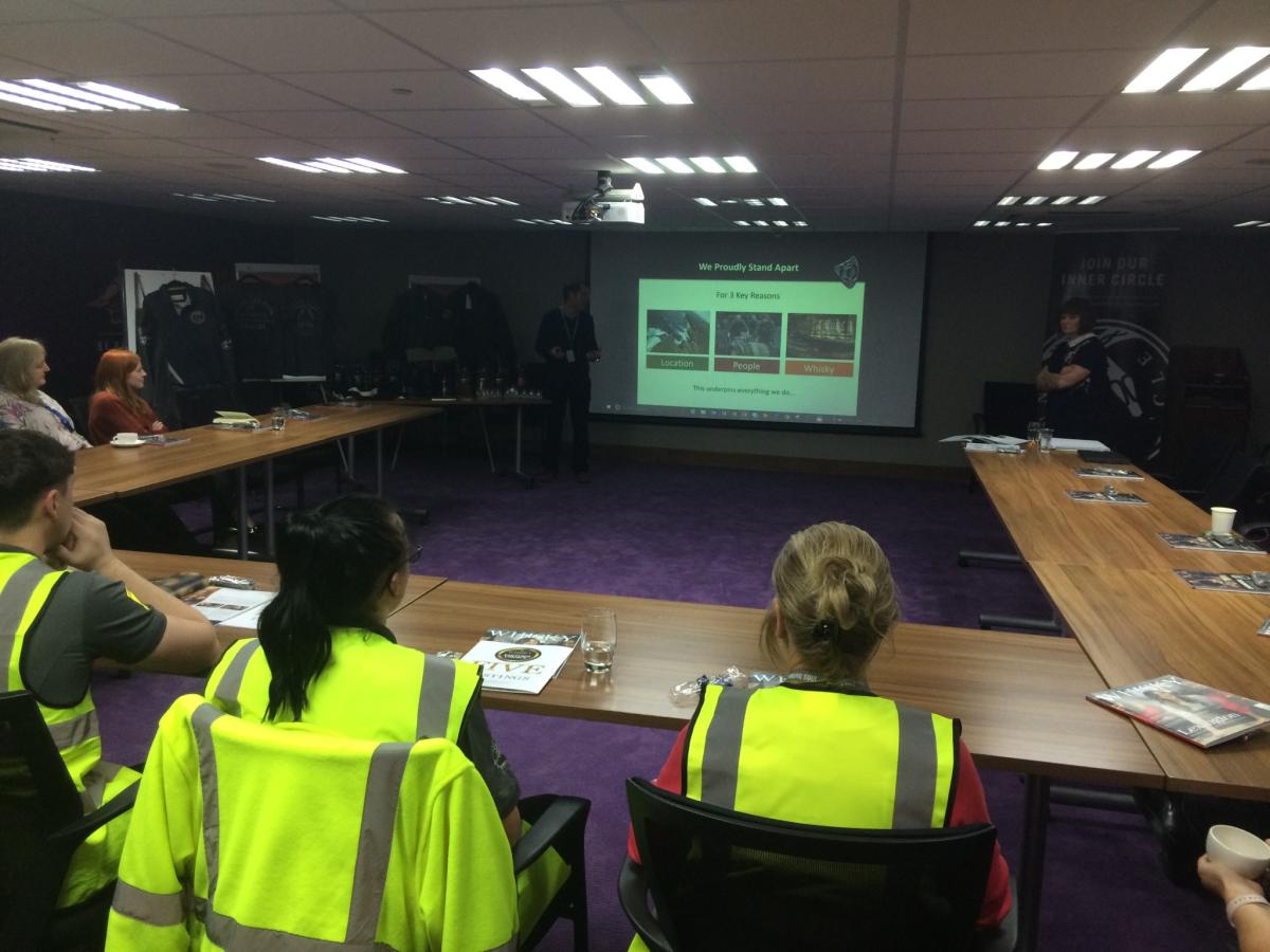 People in hi-vis sitting at a table looking at slides on a screen