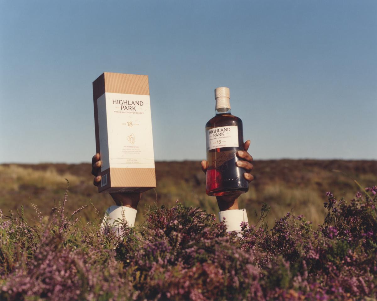 Two hands appearing out of the heather holding Highland Park 18 Year Old pack and bottle