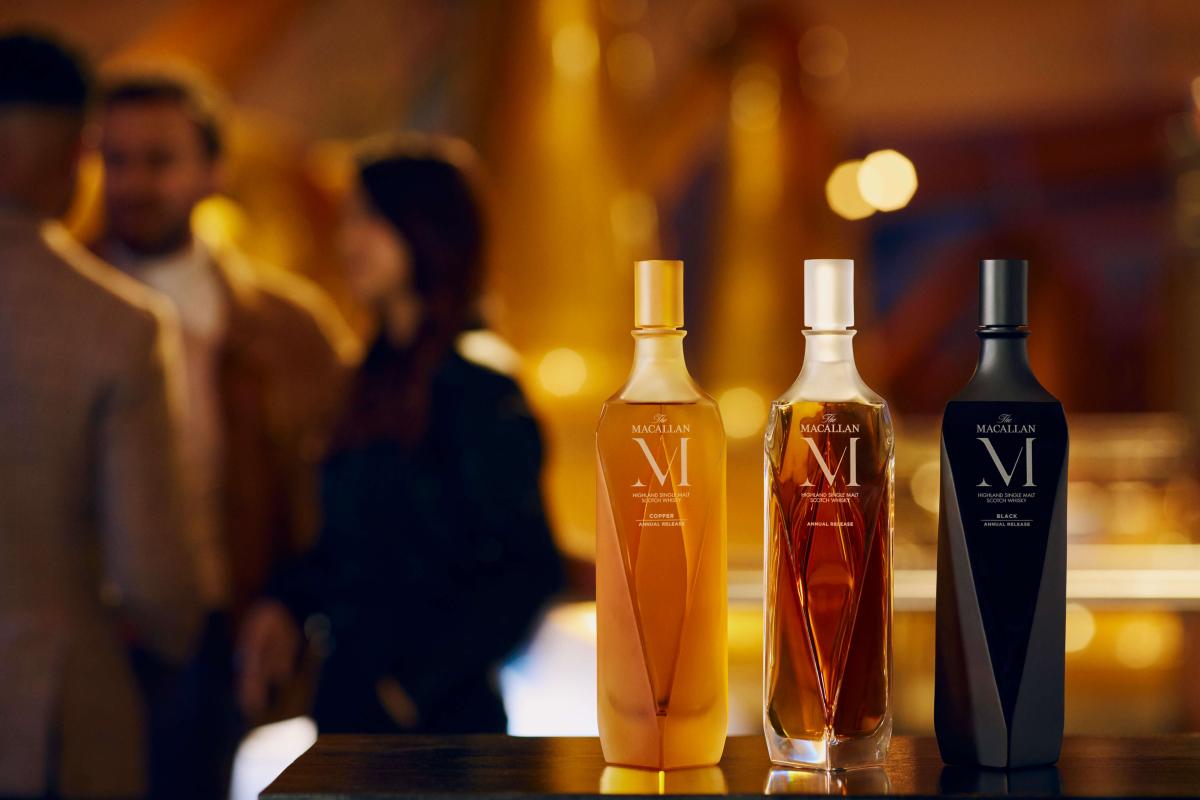 Three Macallan M Collection bottles in the forefront on top of a bar with people in the background