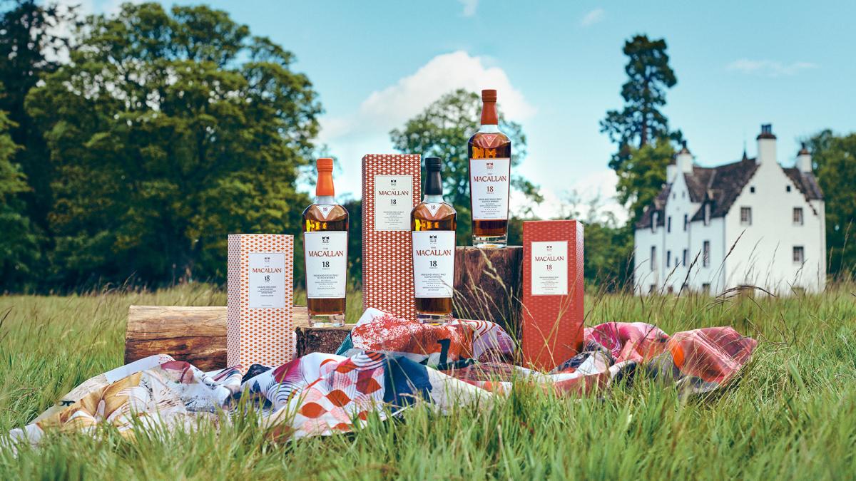 Three bottles of The Macallan outside under a blue sky placed on a picnic blanket in front of a white house