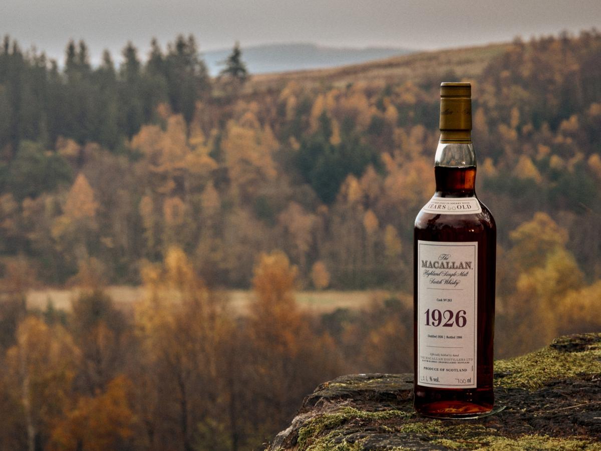 A bottle of The Macallan 1926 on top of a stone with trees at The Macallan Estate in the background