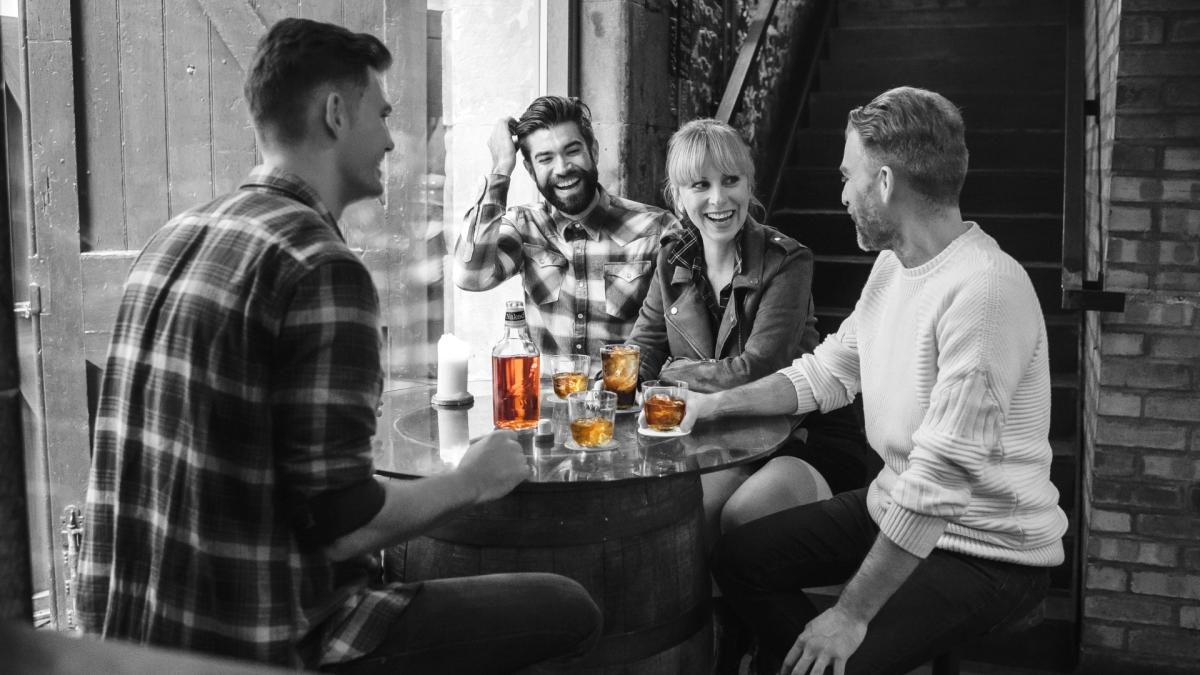 Four people sitting round a table speaking with a bottle of Naked Grouse and drinks in front of them