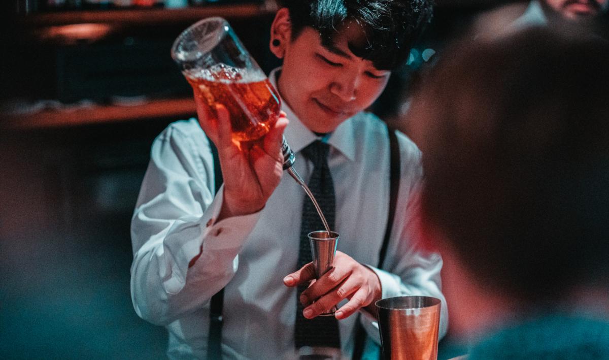 A bartender pouring a cocktail into a glass using a jigger