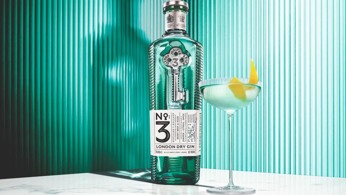 Bottle of No.3 London Dry Gin next to a martini glass in front of a green background