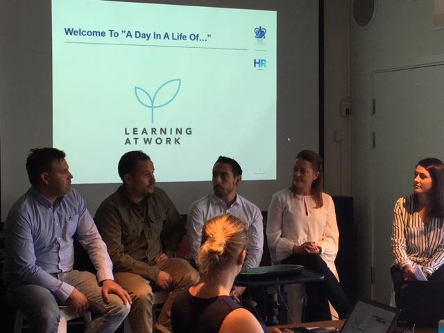 Five people sitting in a row on stage speaking to each other