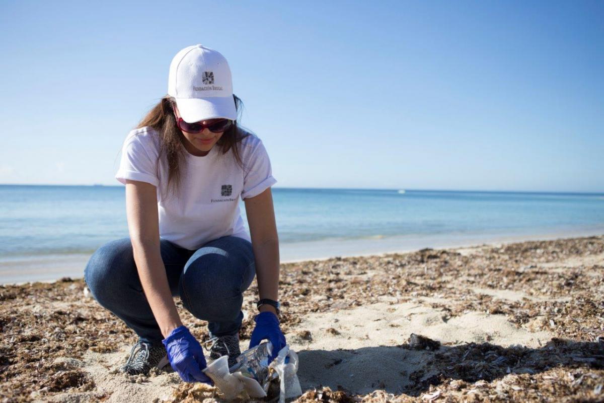 Casa Brugal female employee picking up litter on a beach