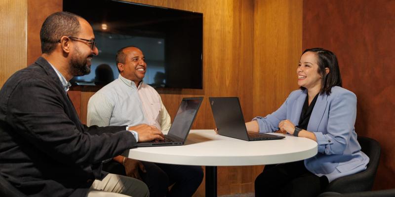 Two men and a women at a table in a meeting room smiling and laughing during a meeting