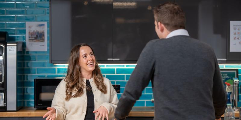 A female colleague talking to a male colleague in a kitchen area