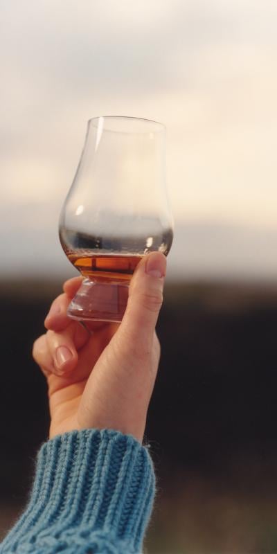 A hand holding up a whisky glass with a measure of whisky inside