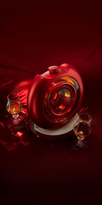 Portrait image of The Macallan TIME:SPACE bottle in front of a deep red background with two whisky glasses next to it